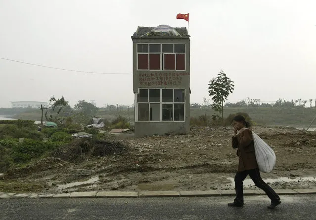 A woman walks past a nail house, the last house in this area, on the outskirts of Nanjing, Jiangsu province, China, October 31, 2008. (Photo by Sean Yong/Reuters)