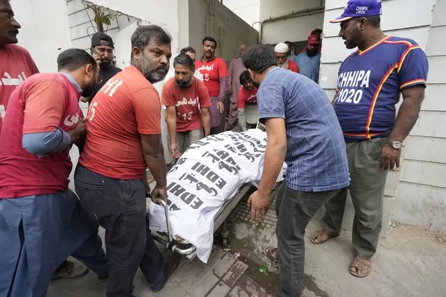 Men carry a body in Karachi, Pakistan, Saturday, November 25, 2023. At least 10 people were killed and 22 injured in the blaze at RJ Mall on Rashid Minhas Road in Karachi. (Photo by Fareed Khan/AP Photo)