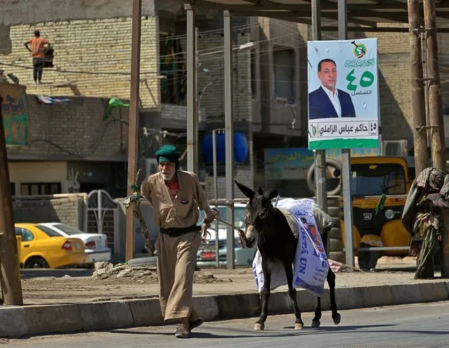A man and his donkey pass by a campaign poster for the upcoming early parliamentary elections in Baghdad, Iraq, Monday, September 20, 2021. (Photo by Hadi Mizban/AP Photo)