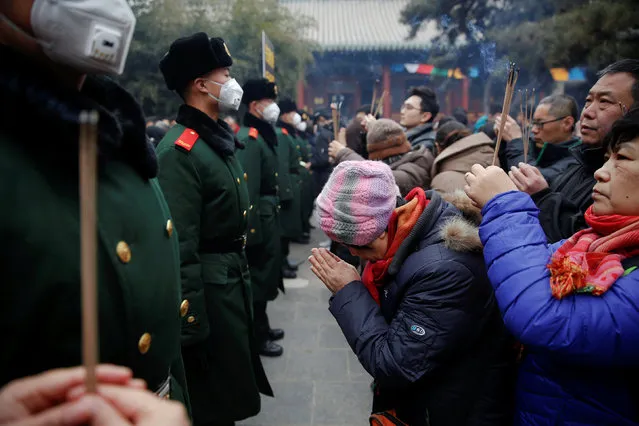 People pray and hold incense sticks in front of paramilitary policemen providing security as people gather at Yonghegong Lama Temple on the first day of the Lunar New Year of the Rooster in Beijing, China January 28, 2017. (Photo by Damir Sagolj/Reuters)