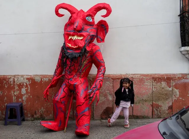 A girls poses next to a pinata shaped like a devil during the annual celebration of the “Burning of the Devil”, a festivity associated with the Feast of the Immaculate Conception which honors the city's patron saint and marking the start of the Christmas season, in Guatemala City, Guatemala on December 7, 2022. (Photo by Sandra Sebastian/Reuters)