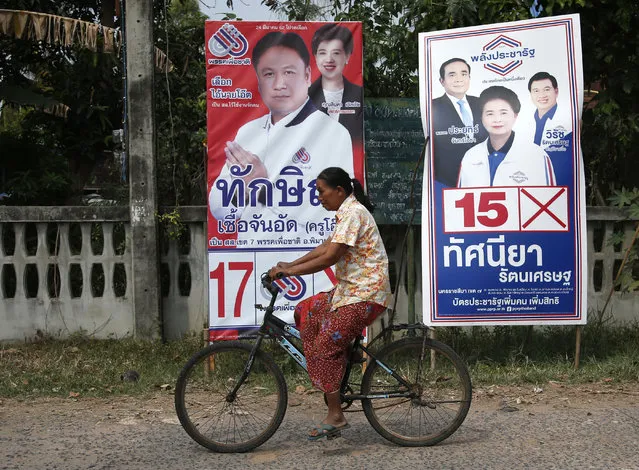 In this March 14, 2019, photo, a Thai woman on a bicycle moves past the posters of Pheu Chart party's Veerawit Chuajunud, left, who changed his name to Thaksin Chuajunud, and Pracha Pracharat Party's candidate and Prime Minister Prayuth Chan-ocha, left on right poster, during an election campaign in Nakhon Ratchasima, Thailand. Thailand’s former Prime Minister Thaksin Shinawatra is in exile and banned from interfering in the country’s politics. But his name is a powerful political attraction and in tribute, and to win votes, some candidates in general election on Sunday, March 24, 2019 have changed their names to Thaksin so supporters of the former leader can register their loyalty at the ballot box. (Photo by Sakchai Lalit/AP Photo)