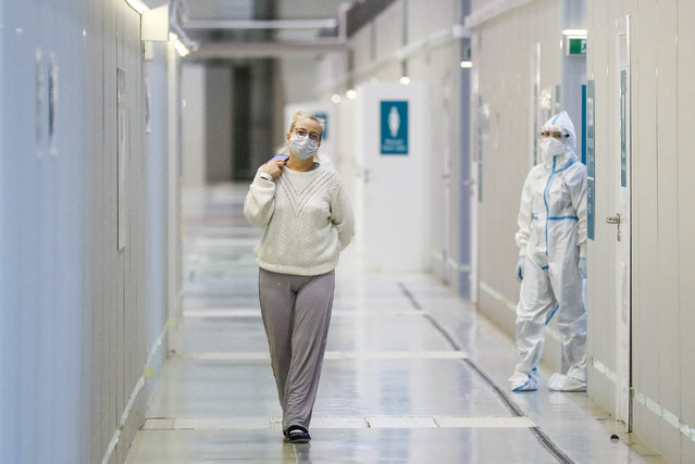 A woman walks past a medical worker in the red zone of a temporary COVID-19 hospital at Pavilion No 75 of the VDNKh Exhibition Centre in Moscow, Russia on November 3, 2021. (Photo by Sergei Savostyanov/TASS)