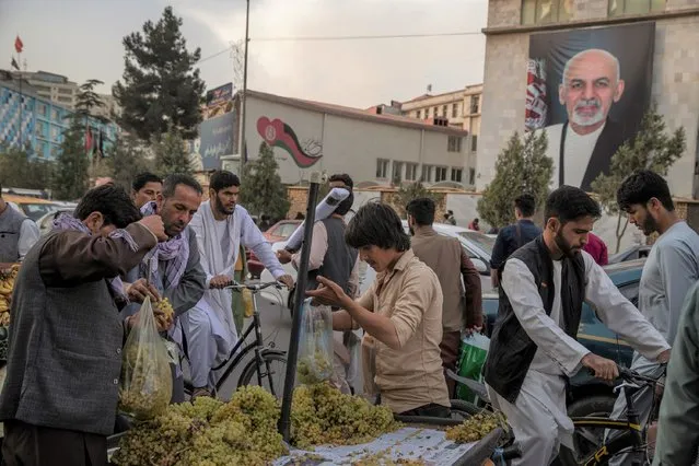Afghans shop for fruit and rush home at days end under a portrait of Afghan President Ashraf Ghani in central Kabul, Afghanistan, Saturday, August 14, 2021. Thousands of internally displaced people flooded into Kabul from the northern provinces in the last few days as the Taliban overran more cities and entire provinces in their military campaign to retake the country as the US withdrawal reaches it's final deadline. (Photo by Victor J. Blue/The Washington Post)