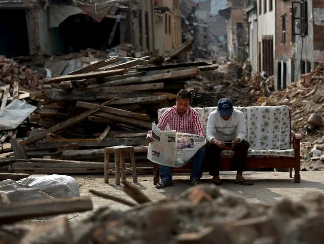 A man reads a newspaper as his friend looks at his mobile phone, as they sit next to collapsed houses on the outskirts of Kathmandu,  Nepal, May 15, 2015. (Photo by Ahmad Masood/Reuters)