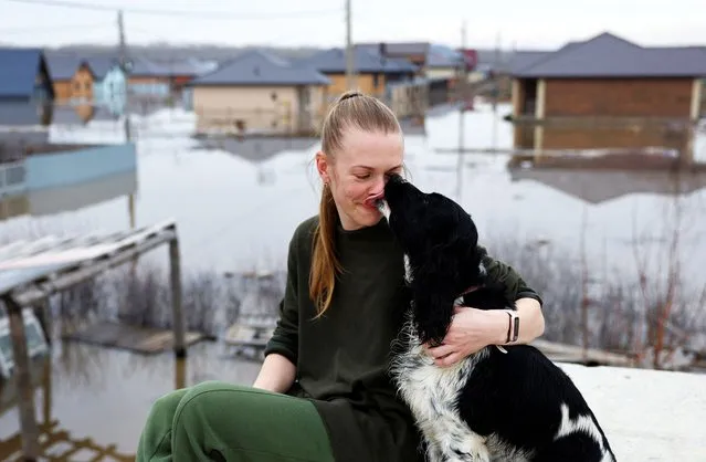 Local resident Yevgenia Perednya pets her dog, as she together with her family escapes the floods, on the roof of unfinished house in the settlement of Ivanovskoye, Orenburg region, Russia on April 10, 2024. (Photo by Maxim Shemetov/Reuters)