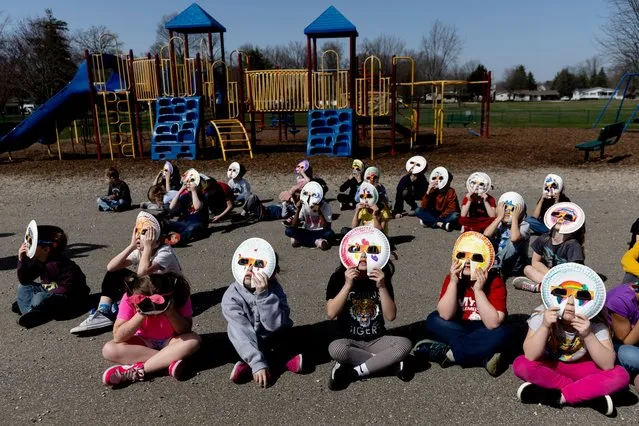 Students from two kindergarten classes, escorted outside by their teachers Amy Johnston and Wendy Sheridan, stare toward the sky with their specially-made glasses to watch the solar eclipse on Monday, April 8, 2024, at Myers Elementary School in Grand Blanc, Mich. The paper plates, which help provide further safety for their eyes, were added on and decorated by each student in their classrooms as a project leading up to the big day. (Photo by Jake May/The Flint Journal via AP Photo)