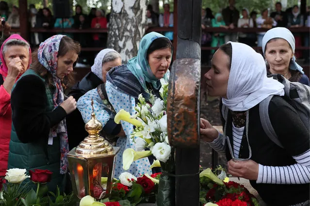 Believers touch a memorial cross at the Ganina Yama Monastery in Sverdlovsk Region, Russia on July 17, 2019, after a religious procession in memory of the Russian royal family. Emperor Nicholas II of Russia and his family were executed on July 17, 1918. The procession is held as part of the Tsar Days Orthodox Culture Festival. (Photo by Donat Sorokin/TASS)