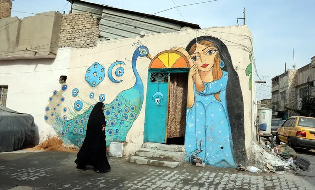 A woman walks past mural in the Al-Anbarieen heritage neighbourhood in Baghdad's Khadimiya city, Iraq, 16 November 2021. The graffiti was made by the Butterfly Effect team, which includes a group of Iraqi painters who volunteered to paint the walls of the houses of heritage neighborhoods of Baghdad, “to beautify the walls of old houses with colors and drawings in order to give hope and happiness and encourage a culture of art and peace in society”, Ali Khalifa one of Butterfly Effect team said. (Photo by Ahmed Jalil/EPA/EFE)