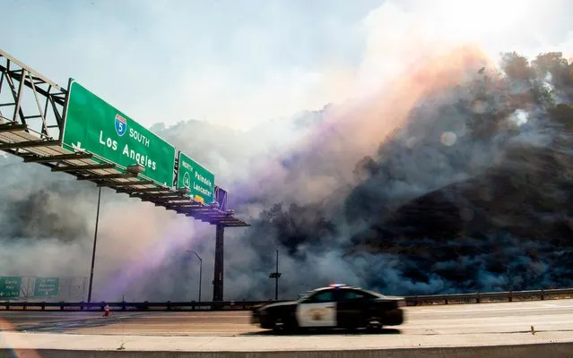 A police car passes by a flaming hillside during the Saddleridge fire in Newhall, California on October 11, 2019. Much of California was on high alert Friday as wind-driven wildfires tore through the state's south, forcing the evacuation of tens of thousands of people and destroying multiple structures and homes. Fire officials said an 89-year-old woman died in Calimesa, about 70 miles (115 kilometers) east of Los Angeles, when fire swept through a trailer park overnight after the driver of a garbage truck that caught fire dumped his burning load nearby. (Photo by Josh Edelson/AFP Photo)