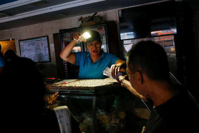 A woman receives money at a food stand using the light of her mobile phone during a power outage affecting Caracas and other regions of the country, in Caracas, Venezuela on August 30, 2024. (Photo by Leonardo Fernandez Viloria/Reuters)