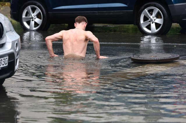 A person jumps into a hole filled with rainwater on a flooded street during heavy rainfall in Berlin, Germany on June 26, 2023. (Photo by Fabrizio Bensch/Reuters)