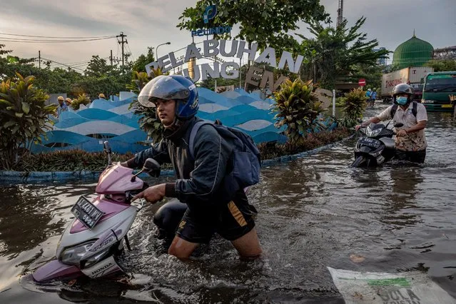 Workers push their motorbikes through the water at the flooded Tanjung Emas container port terminal area, following high tides and broken seawalls, in Semarang, Central Java province, Indonesia on May 23, 2022. (Photo by Aji Styawan/Antara Foto via Reuters)