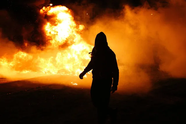 A protester walks in front of a burning barricade outside the Fleury-Merogis prison, near Paris, on April 10, 2017, during a demonstration by prison guards after six of their colleagues were injured by inmates. The protesters started blocking access to the prison during a demonstration on April 10 to protest after six prison guards were assaulted by inmates as they were attempting to break up a fight. (Photo by Geoffroy Van Der Hasselt/AFP Photo)