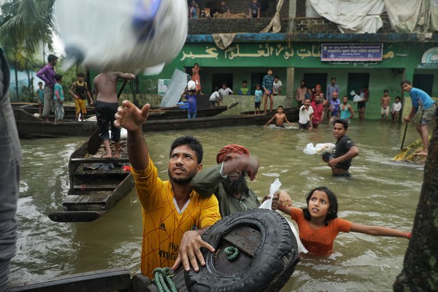 People collect food aid in a flooded residential area following heavy monsoon rainfalls in Companiganj on June 20, 2022. At least 26 more people have died in monsoon flooding and lightning strikes in India, as millions remained marooned in the country and neighbouring Bangladesh, authorities said on June 20. (Photo by Maruf Rahman/AFP Photo)