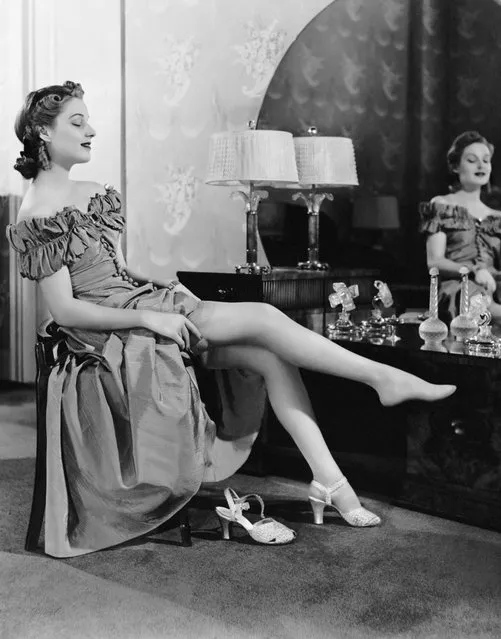 UNITED STATES - CIRCA 1950s:  Woman at dressing table putting on stockings