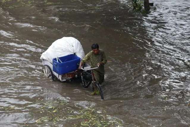 A man wades through flooded water with his tricycle after heavy rains and hailstorm in New Delhi, India, March 14, 2020. (Photo by Anushree Fadnavis/Reuters)