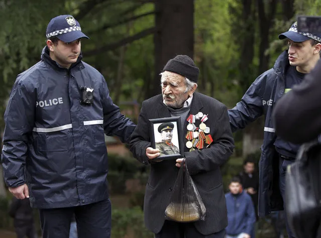 Police officers help Vakhtang Adamashvili, 94, veteran of the WWII with a portrait a portrait of Soviet dictator Josef Stalin to attend a laying ceremony at a war memorial in the Victory Park marking the 75th anniversary of the Nazi defeat in World War II in Tbilisi, Georgia, Saturday, May 9, 2020. (Photo by Shakh Aivazov/AP Photo)