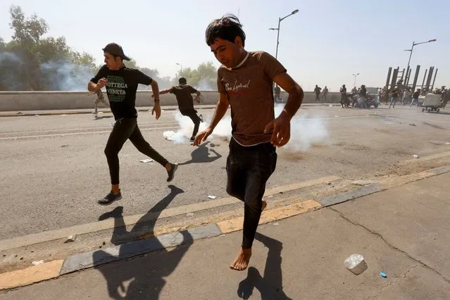 Iraqi protesters run away from tear gas fired by security forces as they gather to mark the third anniversary of the anti-government protests in Baghdad, Iraq on October 1, 2022. (Photo by Ahmed Saad/Reuters)