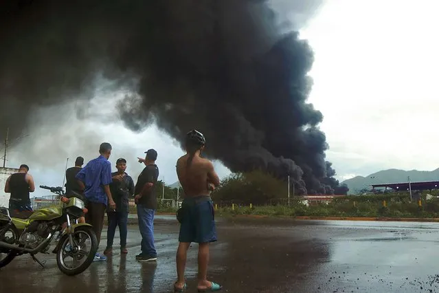 People look at the black smoke from the massive fire at a fuel depot in an oil refining plant of state-owned Petroleos de Venezuela (PDVSA) in Puerto La Cruz, Anzoategui state, Venezuela, on September 19, 2022. (Photo by Carlos Landaeta/AFP Photo)