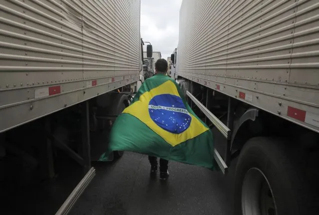 A supporter of President Jair Bolsonaro with a Brazilian flag walks between trucks during a blockade on Castelo Branco highway, on the outskirts of Sao Paulo, Brazil, on November 1, 2022. Supporters of Brazilian President Jair Bolsonaro blocked major highways for a second day as tensions mounted over his silence after narrowly losing re-election to bitter rival Luiz Inacio Lula da Silva. Federal Highway Police (PRF) on Tuesday reported more than 250 total or partial road blockages in at least 23 states by Bolsonaro supporters, while local media said protests outside the country's main international airport in Sao Paulo delayed passengers and led to several flights being cancelled. (Photo by Caio Guatelli/AFP Photo)