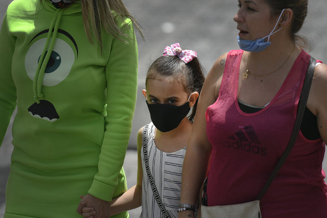 A child wearing a mask amid the new coronavirus pandemic walks with her mother and aunt on Sabana Grande boulevard in Caracas, Venezuela, Wednesday, June 17, 2020. (Photo by Matias Delacroix/AP Photo)