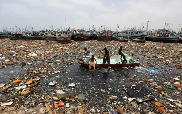 Boys aboard an abandoned boat collect recyclable items through polluted waters in front of fishing boats at Fish Harbor in Karachi, Pakistan, August 17, 2016. (Photo by Akhtar Soomro/Reuters)