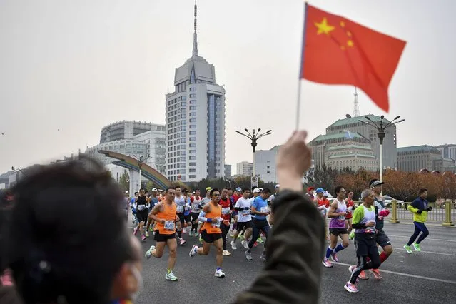 In this photo released by Xinhua News Agency, a spectator waves a national flag as runners compete in the Beijing Marathon in Beijing, Sunday, November 6, 2022. Thousands of runners took to the streets of China's capital on Sunday for the return of the Beijing marathon after a two-year hiatus because of COVID-19, even as another death blamed on China's strict pandemic controls generated more public anger. (Photo by Song Yanhua/Xinhua via AP Photo)