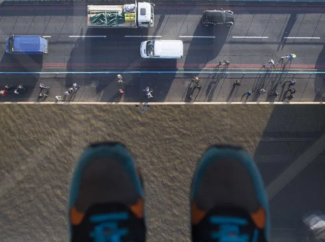 Pedestrians and traffic cross Tower Bridge as viewed through a glass viewing platform on the high-level Walkways during a preview to launch the new viewing experience at the Tower Bridge Exhibition centre in London on November 10, 2014. (Photo by Andrew Cowie/AFP Photo)