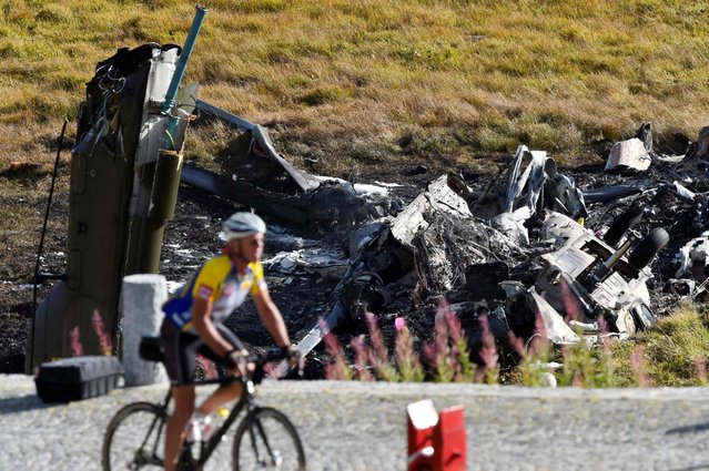 A man cycles past a wreckage of a Swiss army helicopter that crashed, killing two aviators and leaving a third person injured, September 28, 2016 near Gotthard Pass in the Tessin region of the Swiss Alps. (Photo by Michael Buholzer/AFP Photo)