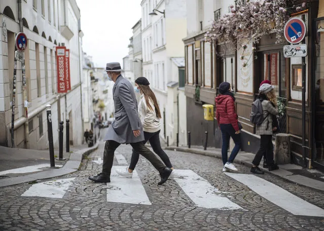 People wearing face masks walk, in the Montmartre district of Paris, Sunday October 25, 2020. A curfew intended to curb the spiraling spread of the coronavirus, has been imposed in many regions of France including Paris and its suburbs. (Photo by Lewis Joly/AP Photo)