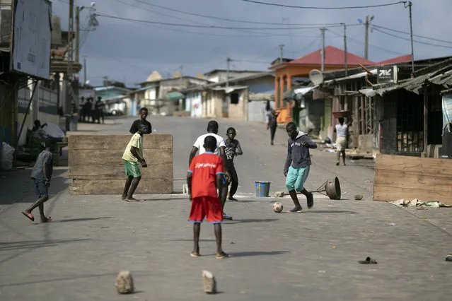 Youth play soccer next to a barricade that was set on a street after protests, earlier this year, against the decision of President Alassane Ouattara's to run for a third term in Bonoua, in the outskirts of Abidjan, Ivory Coast, Friday, October 30, 2020. (Photo by Leo Correa/AP Photo)