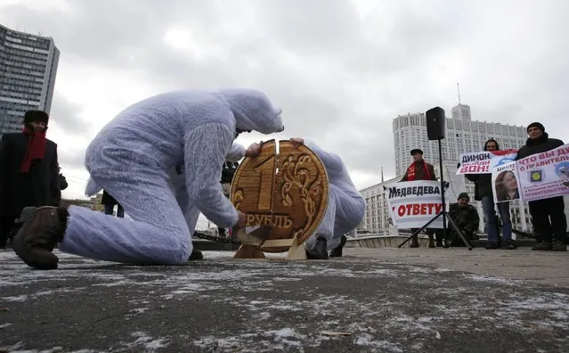 Participants dressed as white bears saw an oversized replica of a one Russian rouble coin as they stage a performance during a rally near the “White House” (R), the headquarters of the federal government, in Moscow, December 22, 2014. Participants, mostly supporters of the Communist Party, protested against the policies conducted by the Russian government and demanded the resignation of Prime Minister Dmitry Medvedev, according to organizers. (Photo by Sergei Karpukhin/Reuters)