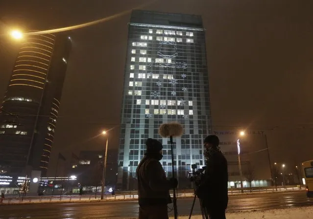 A television crew stands in front of the municipality building lighted up to form the Euro sign in Vilnius December 31, 2014. Lithuania will join euro zone on January 1, 2015. (Photo by Ints Kalnins/Reuters)