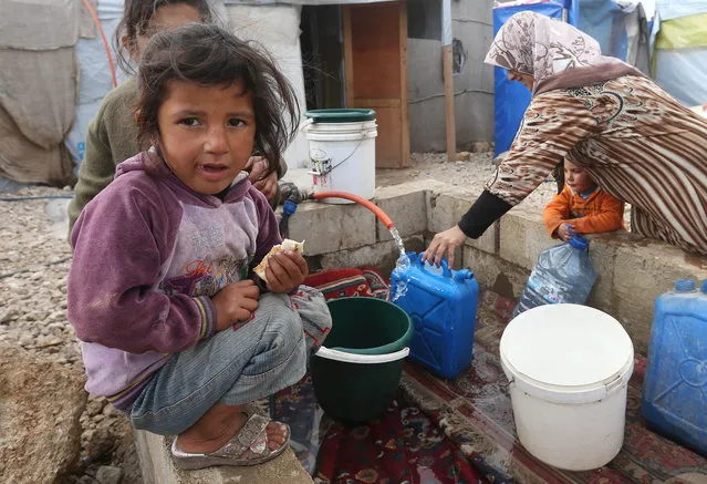 A Syrian girl eats a sandwich as others fill water containers at a refugee camp in Deir Zannoun village, Bekaa valley, Lebanon, Tuesday, January 6, 2015. (Photo by Hussein Malla/AP Photo)