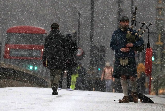 A musician play bag pipes during heavy snowfall on Westminster Bridge as temperatures dropped below freezing in London, Tuesday, February 9, 2021. Snow has swept across the country, with further snowfall predicted, bringing travel problems as temperatures dropped. (Photo by Frank Augstein/AP Photo)