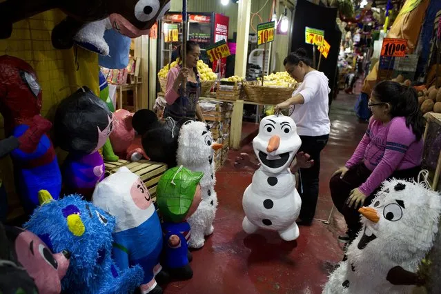 In this January 23, 2015 photo, Jasmin Membrillo, center, accompanied by her daughter Cinthya Jasmin, picks out a piñata representing Disney's Frozen snowman character Olaf, for an upcoming birthday party, at La Merced market in Mexico City. Market vendor Gerardo Moreno Alejo and his wife Edith, at left, sell piñatas and avocados from their stall in La Merced, one of Mexico City's largest markets. (Photo by Rebecca Blackwell/AP Photo)