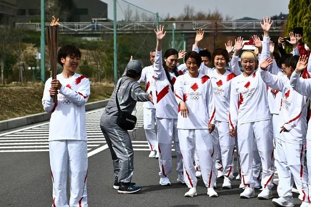 Japanese torchbearer Azusa Iwashimizu (L), a member of the Japan women's national football team, holds an Olympic Torch after passing the flame to the next torchbearer during the torch relay grand start outside J-Village National Training Centre in Naraha town, Fukushima Prefecture, Japan on March 25, 2021. (Photo by Philip Fong/Pool via Reuters)