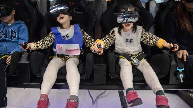 Chinese twins wear virtual reality glasses (VR) as they ride in a roller coaster simulator at the Wantong VR Park, which claims to be China's largest, on November 27, 2016 in Beijing, China. While virtual reality is still seen as a niche technology in many Western countries, VR is flourishing in China as a form of mainstream entertainment. Hundreds of VR arcades, kiosks, cafes, and “experience rooms” are springing up in cities across the country, and offer a VR experience for about the price of a movie ticket. Chinese companies are investing heavily, and some offer VR headsets for as little as US$20 to make VR accessible to the masses. Analysts expect the virtual reality industry in China to boom to US$8.5 billion by 2020, a high-tech surge supported by the government as it seeks ways to diversify the economy away from heavy manufacturing. Chinese president Xi Jinping cited China's development of virtual reality as establishing an “innovative the world economy” during his keynote speech to world leaders at the G20 Summit in September 2016. (Photo by Kevin Frayer/Getty Images)