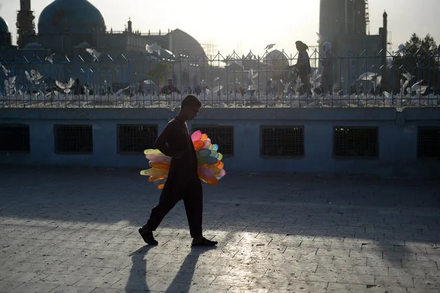 In this photo taken on October 15, 2018, a young Afghan balloon vendor walks as looks for customers in the courtyard of the Hazrat-e-Ali Shrine, or Blue Mosque, in Mazar-i-Sharif. (Photo by Farshad Usyan/AFP Photo)
