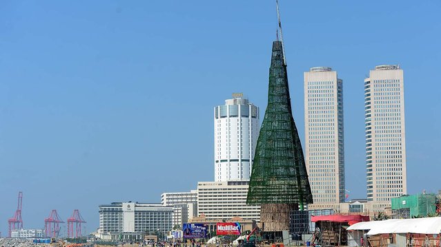 Sri Lankan pedestrians walk past a partially-constructed Christmas tree in Colombo on December 24, 2016. Sri Lanka surpassed the world record for the tallest artificial Christmas tree despite building delays forcing organisers to prune the structure by almost half, an official said. Cricket legend Arjuna Ranatunga initiated plans to build the record-breaking tree in Sri Lanka's capital Colombo, but ran into opposition from the Catholic church which said the money would be better spent on charity. (Photo by Lakruwan Wanniarachchi/AFP Photo)