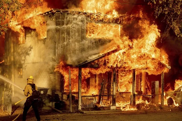 A firefighter sprays water while trying to stop the Sugar Fire, part of the Beckwourth Complex Fire, from spreading to neighboring homes in Doyle, Calif., Saturday, July 10, 2021. Pushed by heavy winds amid a heat wave, the fire came out of the hills and destroyed multiple residences in central Doyle. (Photo by Noah Berger/AP Photo)