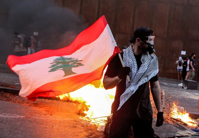 A protester stands with a Lebanese national flag during clashes with army and security forces near the Lebanese parliament headquarters in the centre of the capital Beirut on August 4, 2021, on the first anniversary of the blast that ravaged the port and the city. Hundreds of Lebanese marched on August 4 to mark a year since a cataclysmic explosion ravaged Beirut, protesting impunity over the country's worst peacetime disaster at a time when its economy was already in tatters. (Photo by Patrick Baz/AFP Photo)