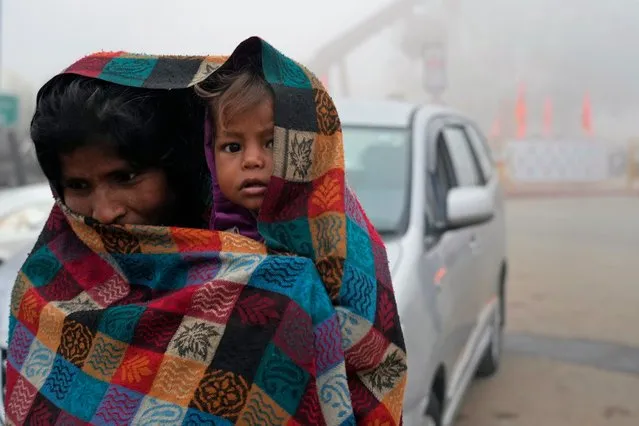 A woman drapes her shawl around a baby as they walk on a cold morning in Ayodhya, India, Friday, December 29, 2023. (Photo by Rajesh Kumar Singh/AP Photo)