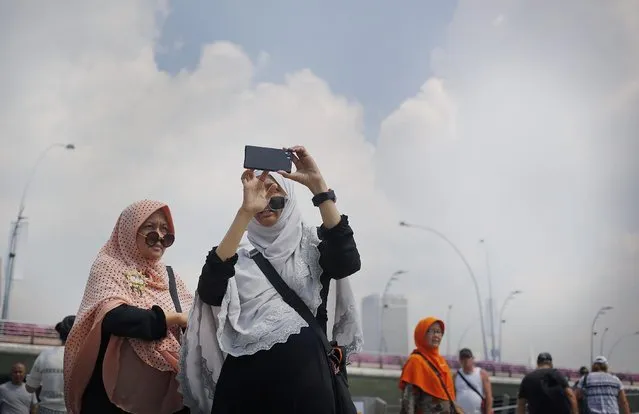 Tourists check photos taken of themselves on their smart phones at a popular tourist spot, Tuesday, April 21, 2015, in Singapore. (Photo by Wong Maye-E/AP Photo)