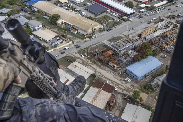 Australian Federal Police Tactical Response officer inspects the damage over the Chinatown area from the air during an operation in Honiara, Solomon Islands, Wednesday, December 1, 2021. New Zealand announced Wednesday that they will send up to 65 military and police personnel to the Solomon Islands over the coming days after rioting and looting broke out there last week. (Photo by Gary Ramage via AP Photo)
