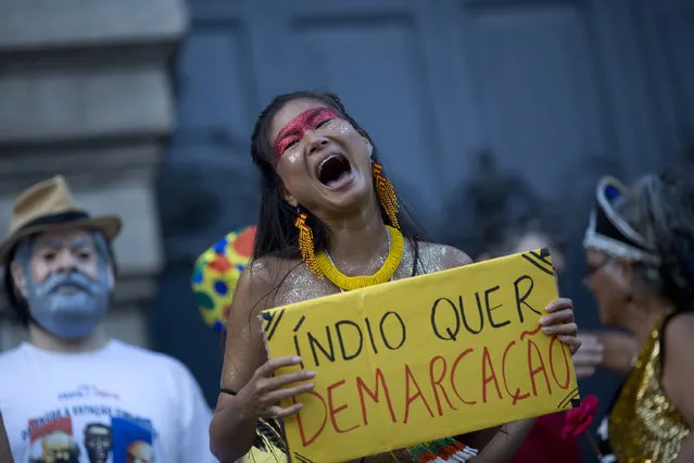 A reveler holds a sign that reads in Portuguese: “Indians want demarcation” during the “Out Temer” carnival street party in Rio de Janeiro, Brazil, Friday, February 24, 2017. Merrymakers took to the streets to protest Brazil's President Michel Temer. (Photo by Silvia Izquierdo/AP Photo)