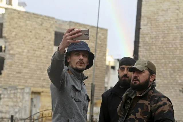 A man takes a selfie with rebel fighters in front of a rainbow in the rebel held area of Aleppo's Salah al-Din neighbourhood, Syria March 28, 2016. (Photo by Abdalrhman Ismail/Reuters)