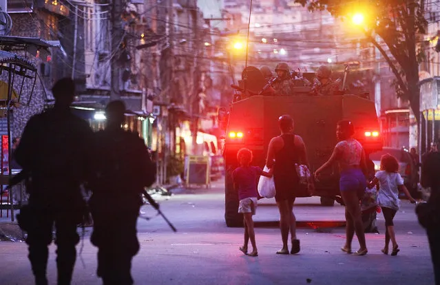 People walk as Brazilian Navy soldiers in a tank enter the unpacified Complexo da Mare, one of the largest 'favela' complexes in Rio, on March 30, 2014 in Rio de Janeiro, Brazil. The Brazilian government has deployed federal forces to occupy the group of violence-plagued slums ahead of the June 12 start of the 2014 FIFA World Cup. (Photo by Mario Tama/Getty Images)