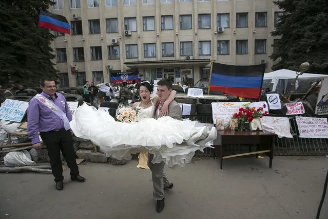A pair of bride and groom poses for photos in front of barricades set up outside a regional government building seized by pro-Russian armed men in Kramatorsk, eastern Ukraine April 22, 2014. An international agreement to avert wider conflict in Ukraine was faltering on Monday, with pro-Moscow separatist gunmen showing no sign of surrendering government buildings they have seized. (Photo by Baz Ratner/Reuters)